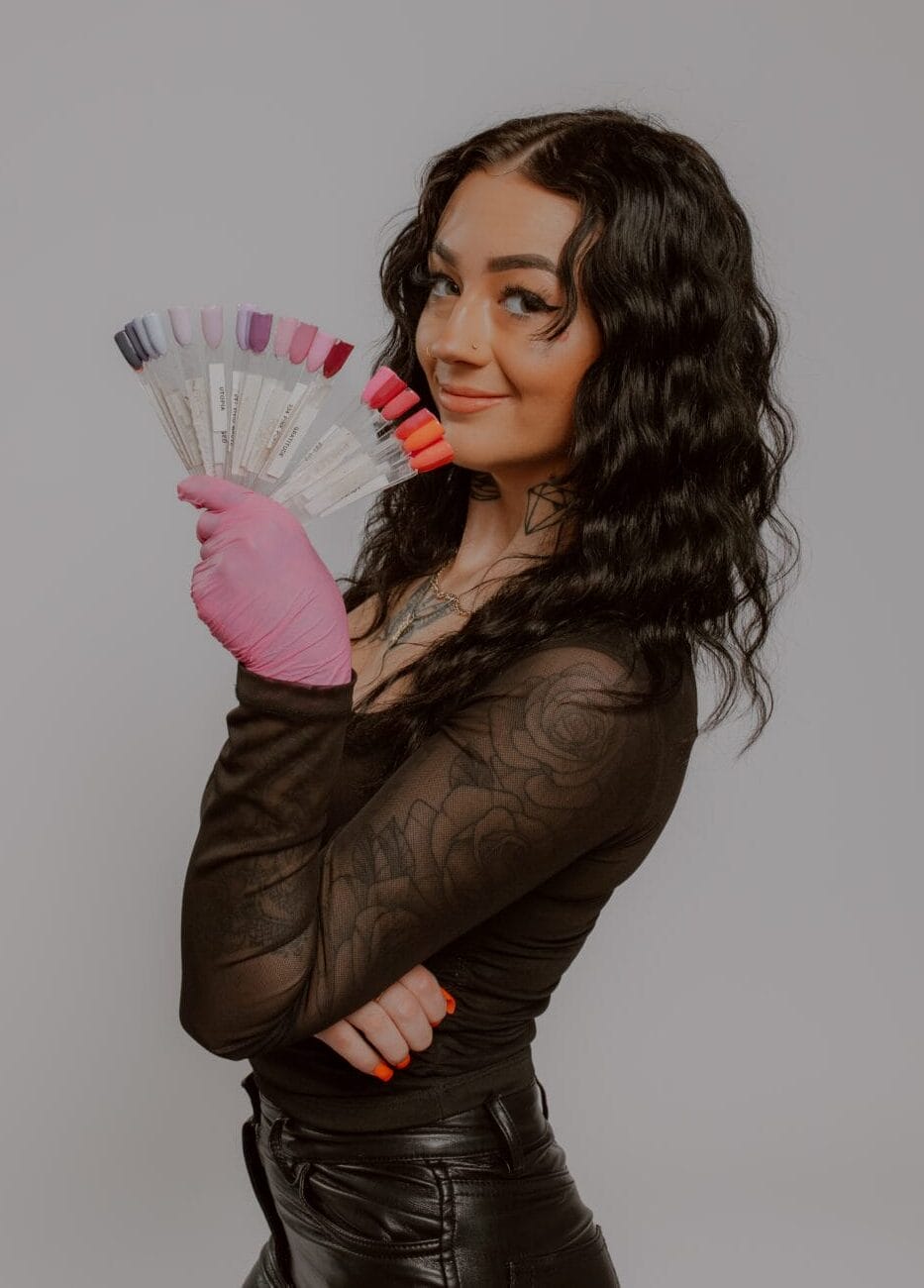 Smiling nail technician at YOLOve beauty salon displaying colorful nail polish samples for manicure services
