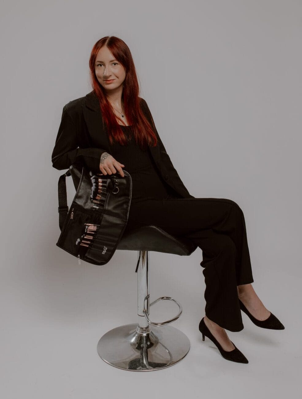 Professional beauty stylist with vibrant red hair sitting in salon chair with makeup kit at YOLOve beauty Dartmouth