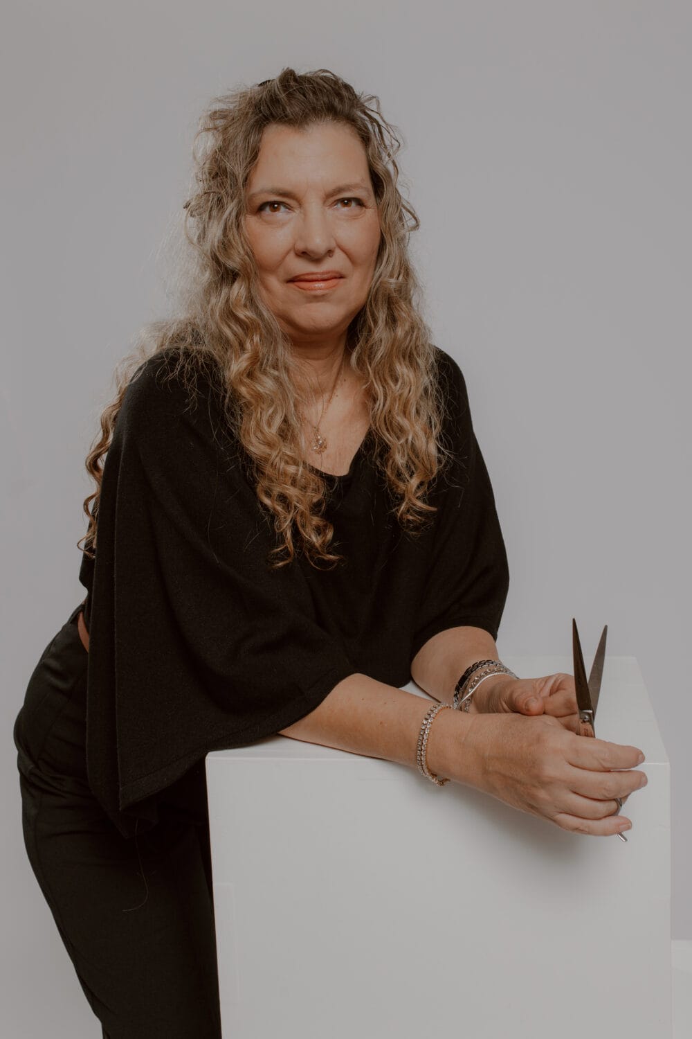 Professional hair stylist with beautiful curly blonde hair holding scissors at YOLOve Beauty salon in Dartmouth