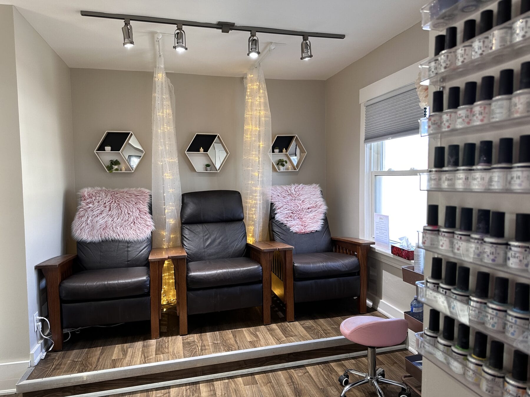 Luxurious pedicure station with three black leather chairs, pink fuzzy pillows, and nail polish wall at YOLOve beauty